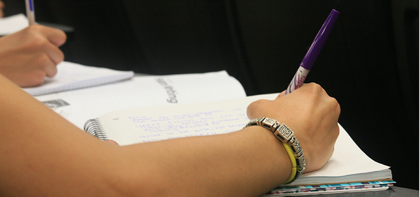 A hand is seen writing in a notebook.