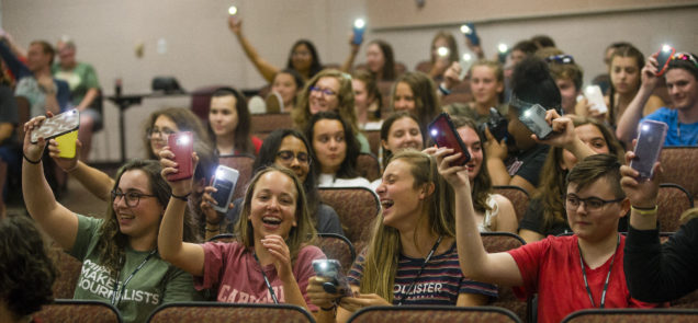 Participants hold up their phones with the flashlight on during the MIPA's Got Talent variety show during the 2019 MIPA Summer Journalism Workshop.