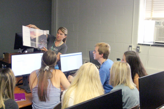 Grand Blanc High School yearbook adviser Ava Butzu holds up a book while talking to students at the MIPA Summer Journalism Workshop, where she is an instructor.