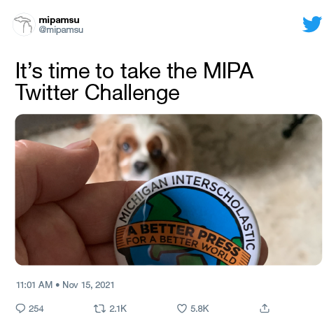Screen shot of a MIPAMSU Twitter post featuring a dog staring at Michigan Interscholastic Press Association button pin held in a hand.