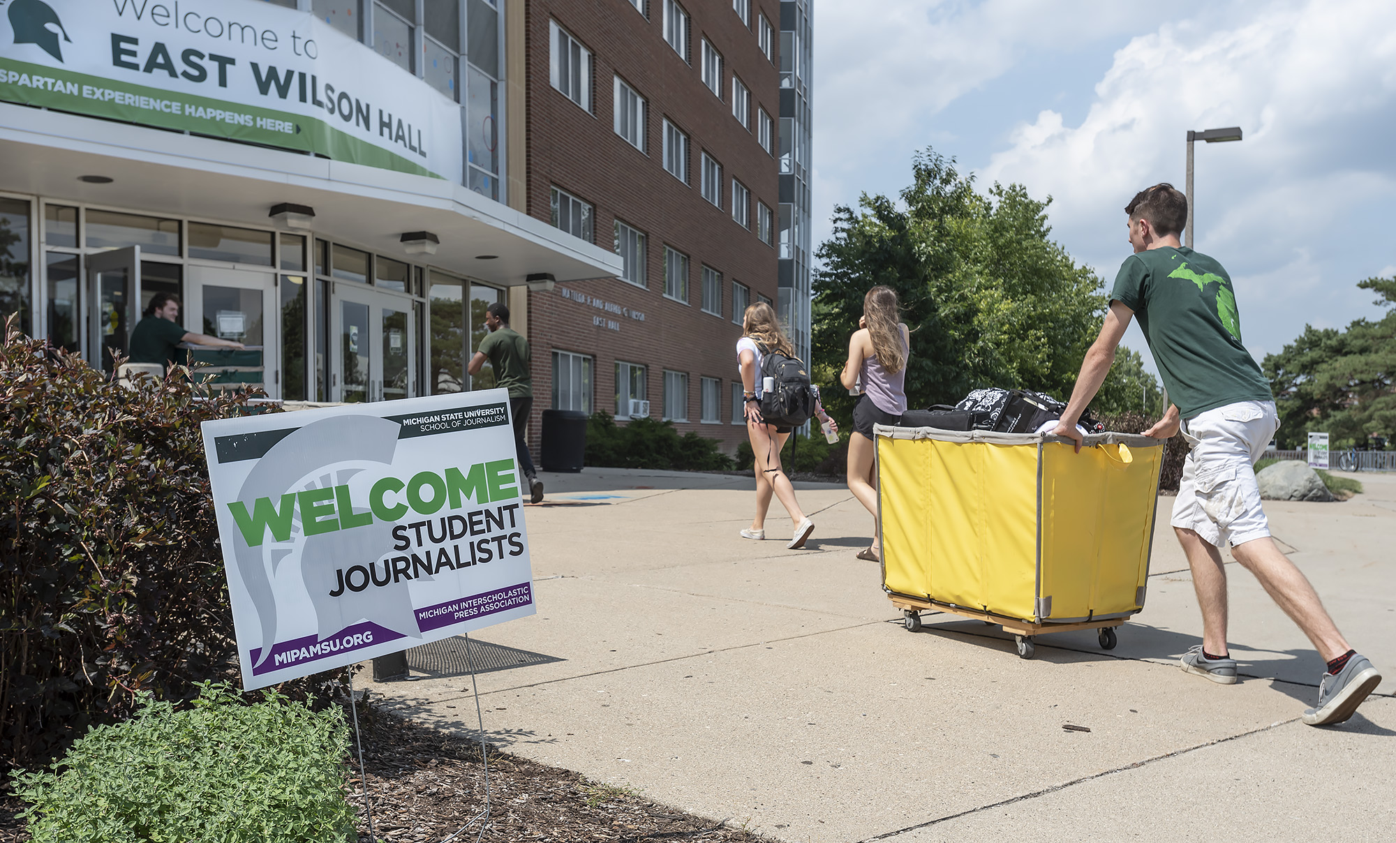 Participants push a rolling cart of items into an MSU residence hall during move-in