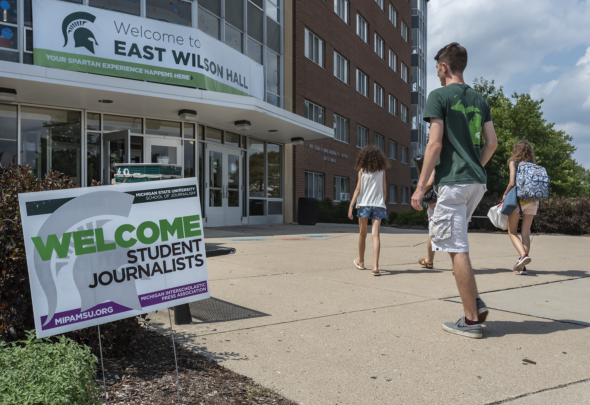 Students walk into an MSU residence hall, past a sign that says Welcome Student Journalists