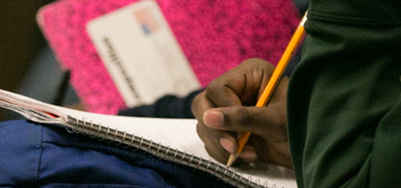 Hand holding a pencil and writing in a notebook